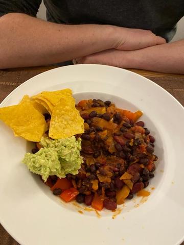 Photo of a bowl of vegan bean chilli with tortilla chips and guacamole