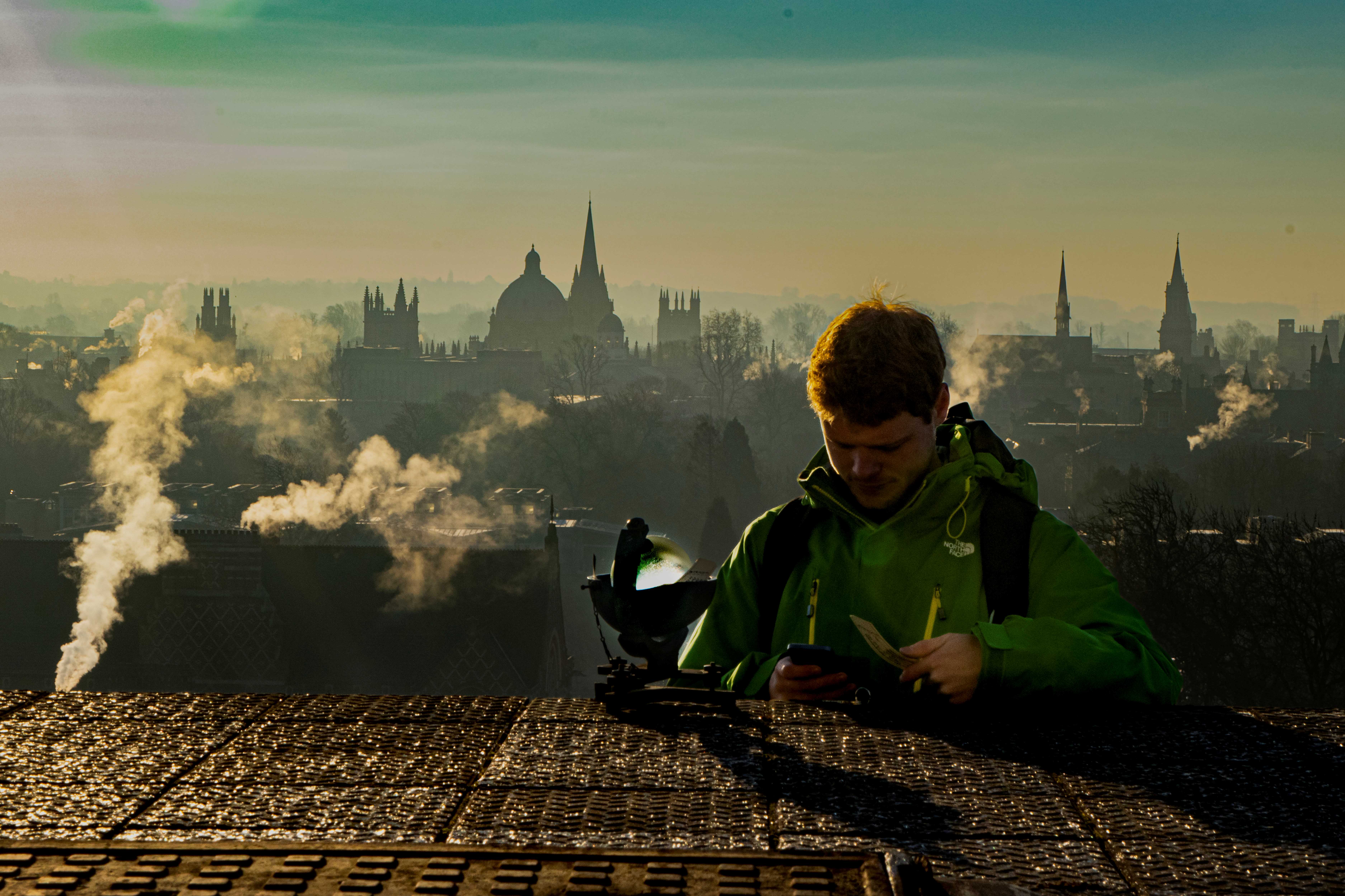 A person with measuring equipment on a roof with Oxford city in the background.